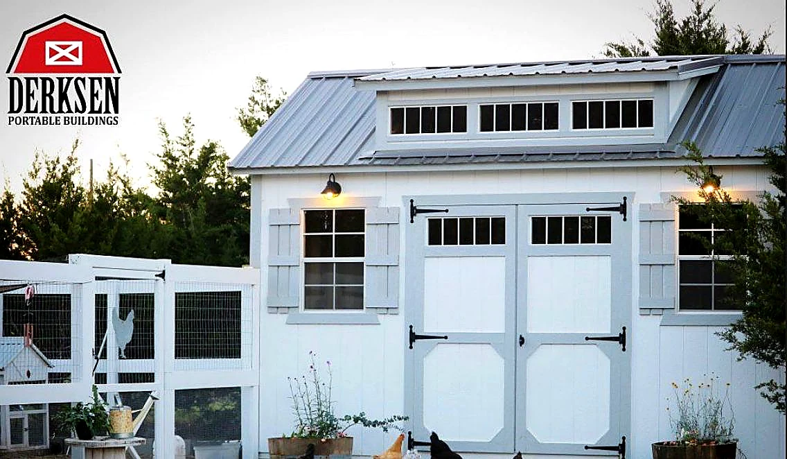White Derksen Portable Building lofted barn with dark grey metal gambrel roof and Derksen Portable Buildings dealer signage on a Larkin's Portable Buildings Nebraska lot.